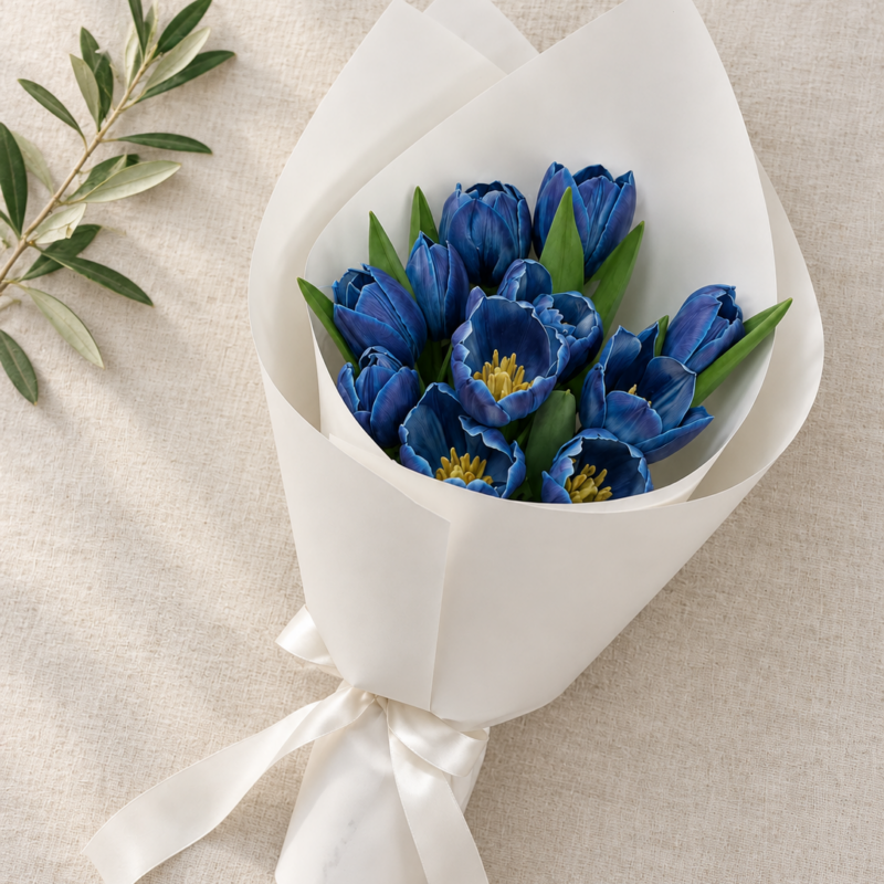 12 blue tulips in white wrapping with a matching white ribbon, on cream linen