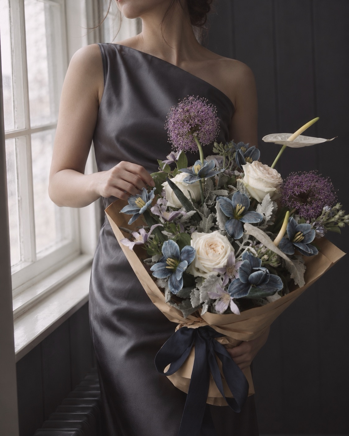 Woman holding a blue tulip and ivory rose bouquet with white anthurium, purple alliums and silver foliage